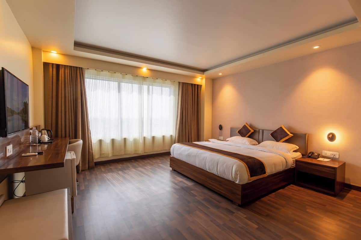 Habitación de hotel con una cama grande, mesitas de noche, un escritorio con silla, televisión y una ventana con cortinas.