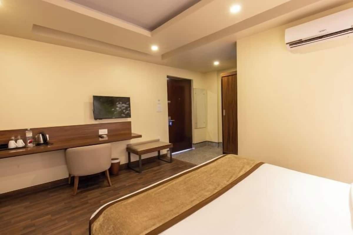 Una habitación de hotel con cama, escritorio con silla, televisor y aire acondicionado.