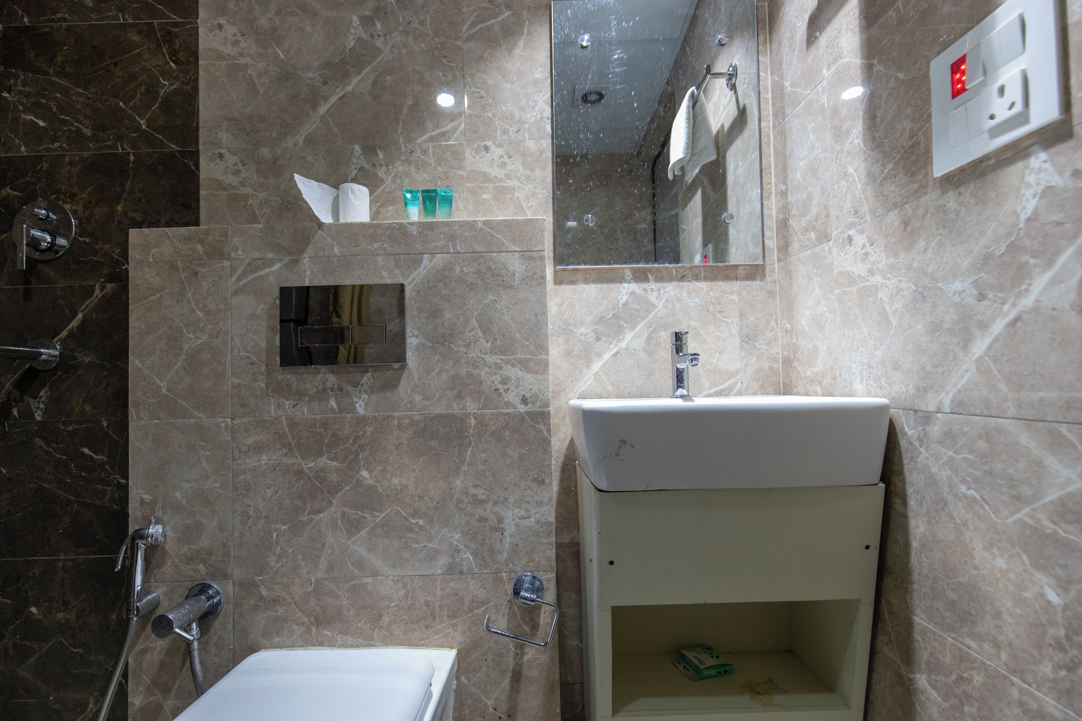 Un baño con pared de mármol, lavamanos blanco, espejo y ducha.