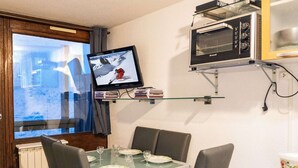 A dining area with a table set for four, a television mounted on the wall, and a microwave shelf above the table. - Modern Apt in Val Thorens - 4 Pers, Balcony, Ski-In/Ski-Out, Near Shops & Restaurants (Val Thorens)