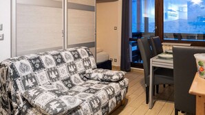 A cozy living area with a patterned sofa, a dining table with chairs, and a view through a window. - Modern Apt in Val Thorens - 4 Pers, Balcony, Ski-In/Ski-Out, Near Shops & Restaurants (Val Thorens)