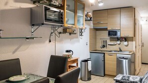 A compact kitchen with a built-in oven, microwave, and a small refrigerator. There is a dining area with a table and chairs, and a sofa with patterned cushions. - Modern Apt in Val Thorens - 4 Pers, Balcony, Ski-In/Ski-Out, Near Shops & Restaurants (Val Thorens)