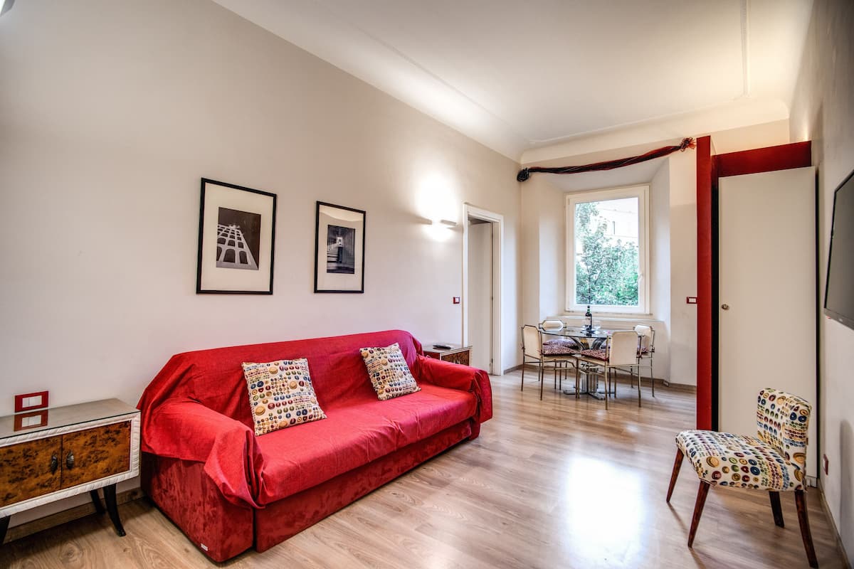 Un salon avec un canapé rouge, un meuble en bois et un coin repas comprenant des chaises et une table.