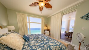 A bedroom with a bed, a ceiling fan, a window with curtains, and a view of the ocean. - Big Balcony beach front corner unit. Next to county pier. 4 Beach chair service! (Panama City Beach)