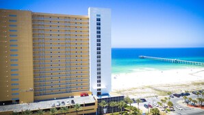 A hotel with multiple floors and balconies, a beach with a pier, and clear blue skies. - Big Balcony beach front corner unit. Next to county pier. 4 Beach chair service! (Panama City Beach)