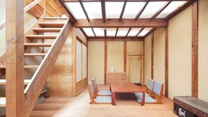 A room with a wooden staircase, a dining table with chairs, and a traditional Japanese-style room with tatami mats. - Kumeya (Komoro)