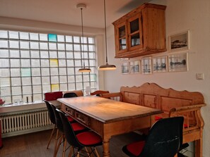 A dining area with a wooden table, red chairs, a wooden bench, and a window with a grid pattern. - Vacation home for 6 people located directly on the dune (Wangerooge)