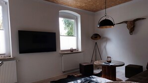 Ett modernt vardagsrum med en platt-TV, ett träpanelat tak, ett stort fönster och en dekorativt upphängd tjotskalle.