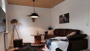 Ett mysigt vardagsrum med en brun lädersoffa, ett runt soffbord i trä, en svart lampa och en matta av kohud.
