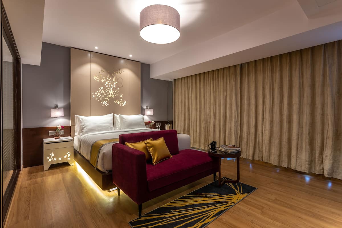 Quarto de hotel moderno com uma cama grande, um sofá vermelho, uma mesinha e um objeto decorativo na parede.