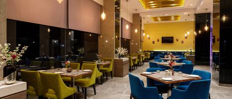 A modern restaurant with a mix of green and blue chairs, marble flooring, and a central counter.
