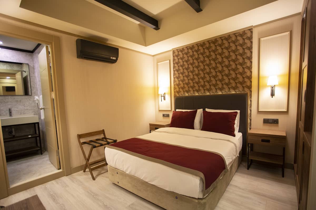 A hotel room with a bed, bedside tables, a mirror, and a bathroom visible through an open door.