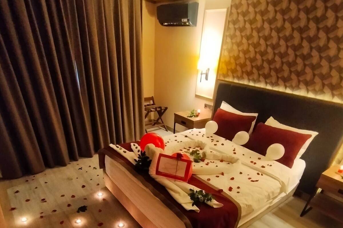 A hotel room with a neatly made bed, a bedside table with a lamp, and a wall-mounted air conditioner.