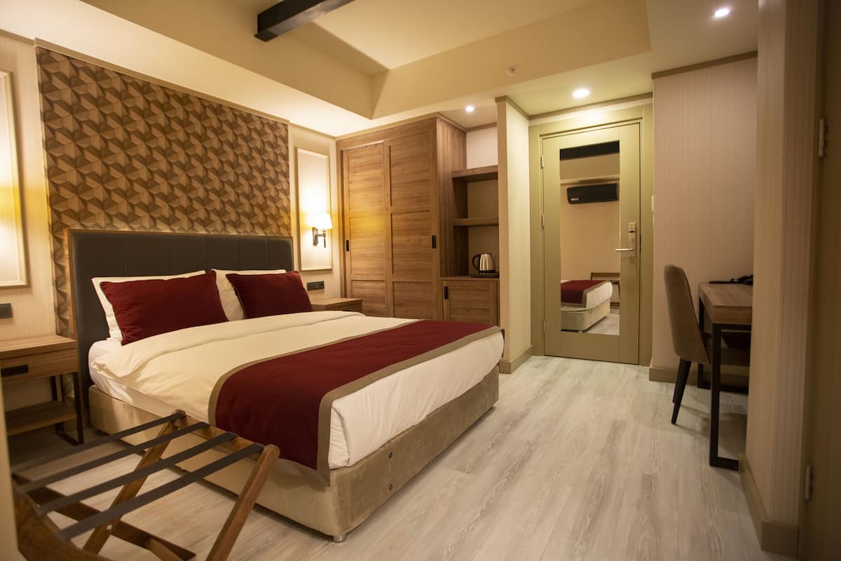 A modern bedroom with a large bed, wooden wardrobe, bedside tables, and a desk with a chair.