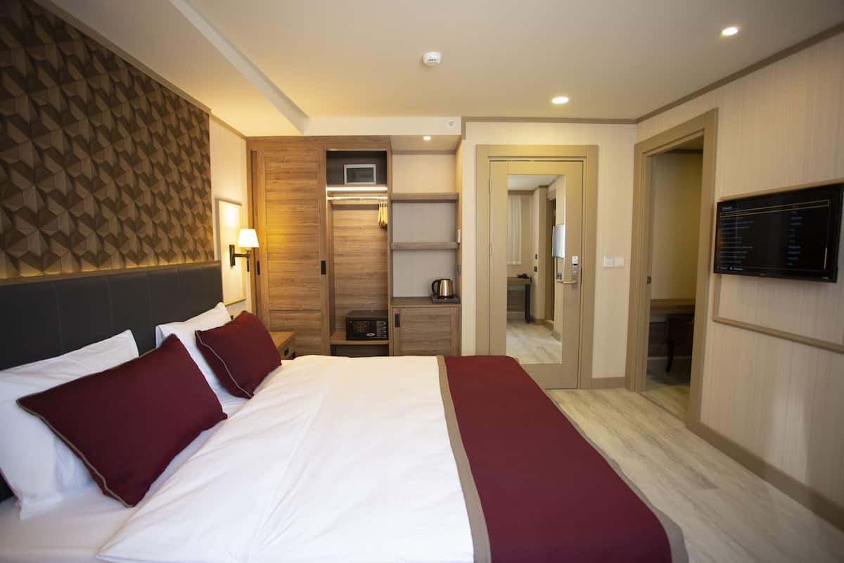 A hotel room with a large bed, a wooden headboard, a built-in TV, a microwave, and a small kitchenette.