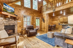 Cozy cabin interior with a stone fireplace, comfortable seating area, and fully equipped kitchen.