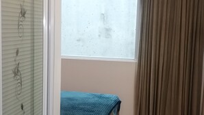 Ein Schlafzimmer mit Bett, Fenster, Vorhang und Tür mit Milchglasfenster.