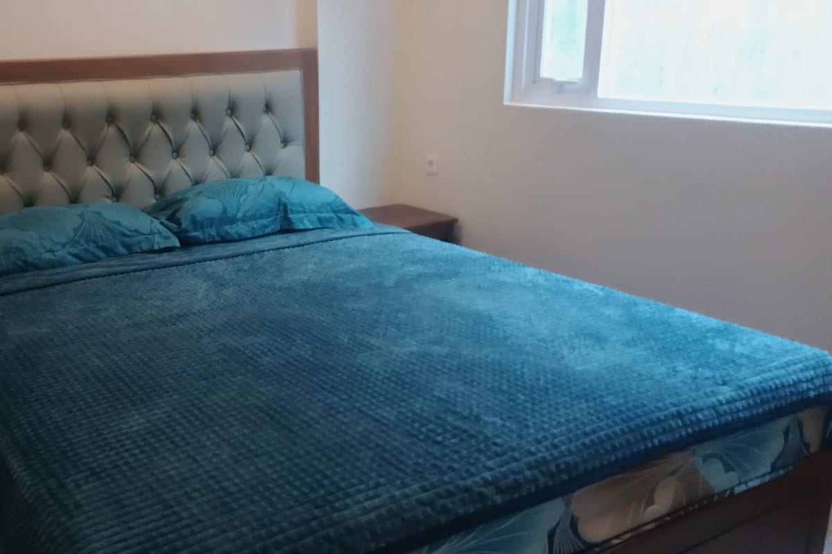 Ein Bett mit einem mit Knöpfen besetzten Kopfteil, zwei passende Kissen und eine blaue Decke.
