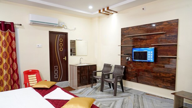 A hotel room with a bed, a desk, a chair, a TV, and an air conditioning unit.