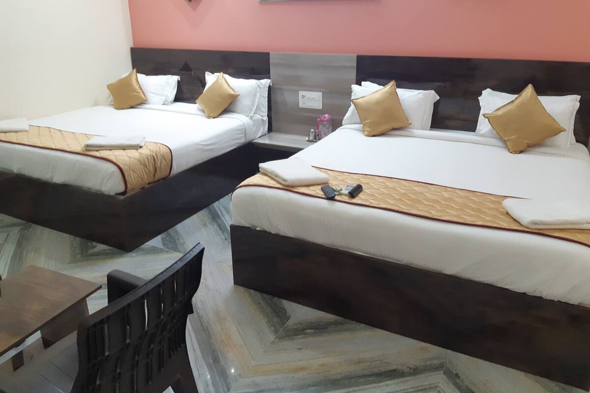 Une chambre d’hôtel avec deux lits, chacun doté d’une tête de lit en bois, de draps blancs et d’oreillers dorés. On aperçoit une petite table avec une chaise au premier plan.