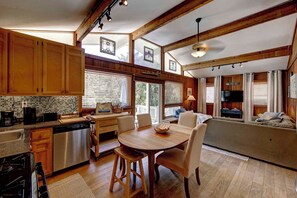 A spacious kitchen with wooden cabinets, a dining table with chairs, a built-in oven, and a large window with blinds. - Sandy Pause - Ocracoke Island (Ocracoke)