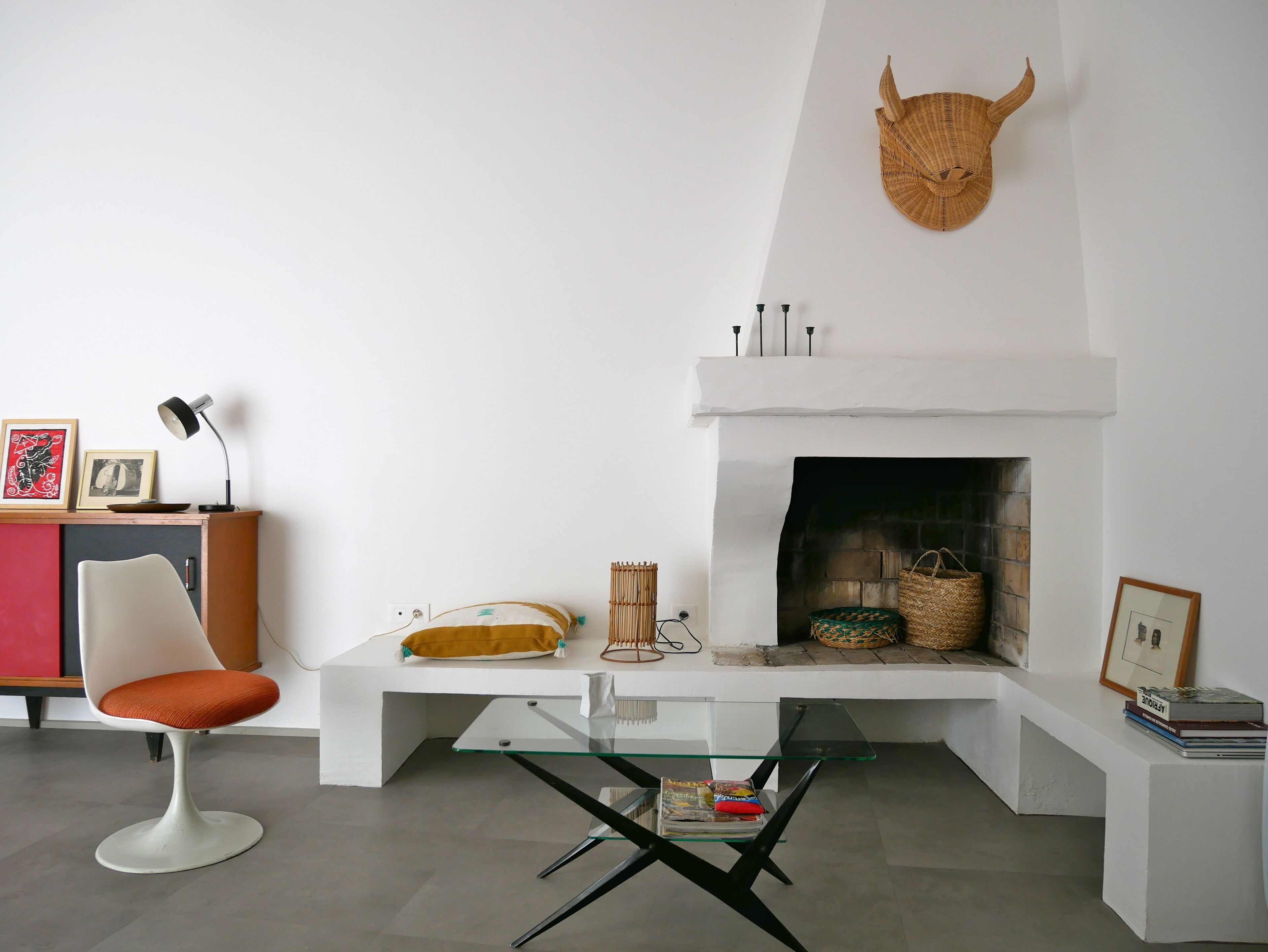 Un salon moderne avec une cheminée blanche, une table basse en verre, un canapé blanc et un fauteuil rouge.