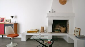 Un salon moderne avec une cheminée blanche, une table basse en verre, un canapé blanc et un fauteuil rouge.