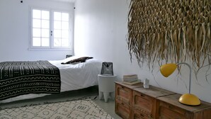 Une chambre à coucher avec un lit, une table de chevet avec des livres, une lampe et une plante suspendue.