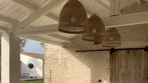Un intérieur moderne avec un mur en pierre, des poufs en fibres tressées, un banc en bois et des lampes suspendues en osier.