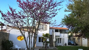 Une maison moderne à l’extérieur blanc, avec une terrasse dotée de chaises blanches et un arbre aux fleurs roses.