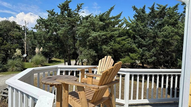 Une terrasse en bois, agrémentée d’une table et de chaises, entourée d’une balustrade blanche, et offrant une vue sur une zone boisée.