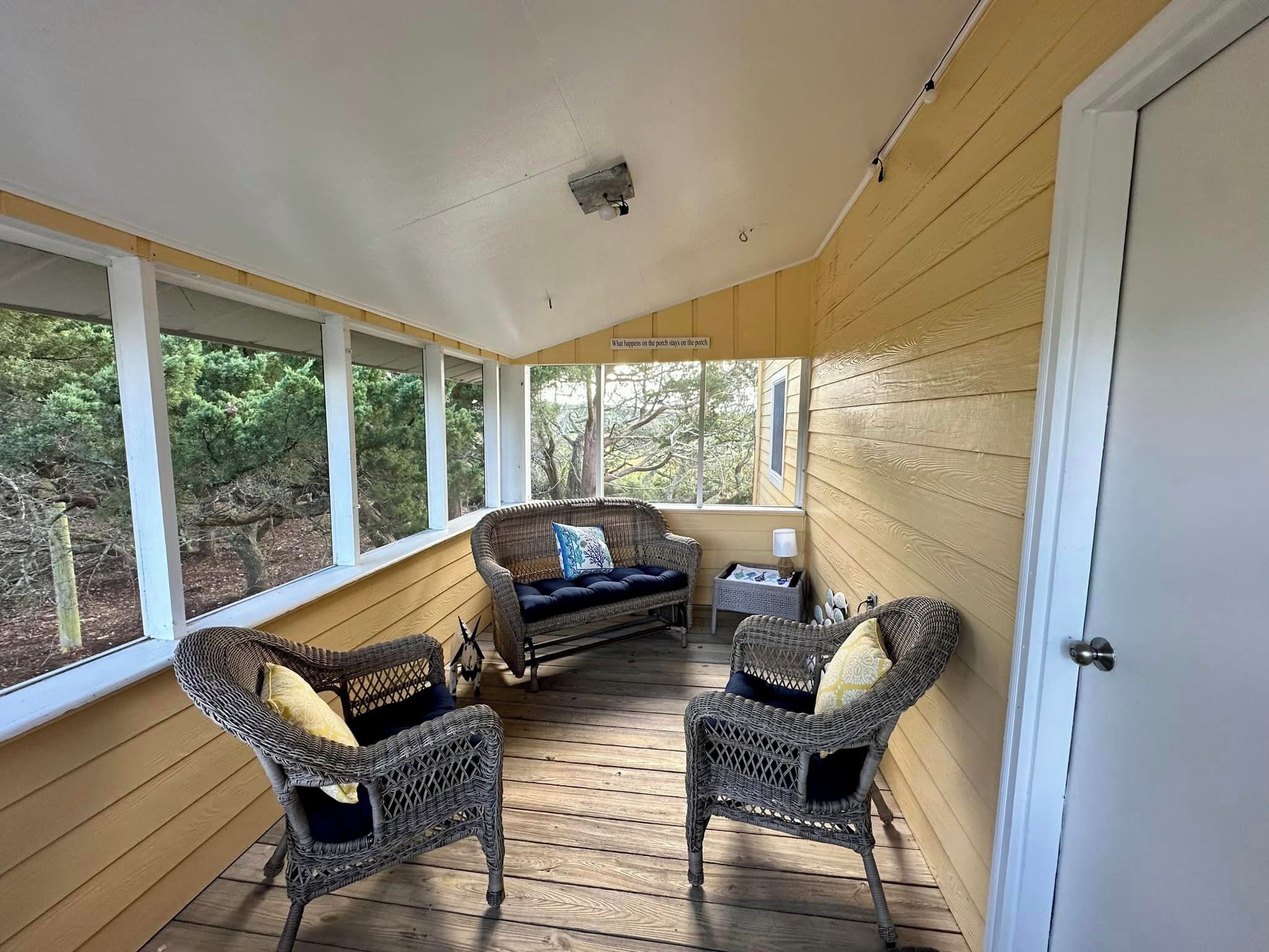 A covered porch with wicker furniture and a view of trees.