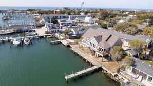 A marina with docked boats, a waterfront property with a large house, and a lighthouse in the background.