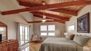 Un dormitorio con techo de madera, una cama, un aparador, una silla y un cuadro en la pared.