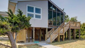 Una casa de dos pisos con un ventanal grande, una terraza de madera y una escalera.