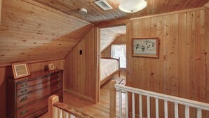 Un intérieur en bois avec une chambre en mezzanine, une commode et un tableau encadré au mur.