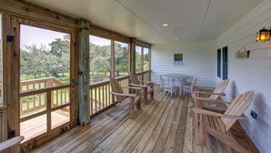 Une véranda couverte avec des balustrades en bois, une table avec des chaises et une vue sur l’extérieur.