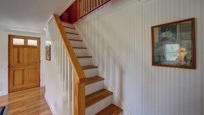 Un escalier en bois, avec des murs recouverts de panneaux blancs et un tableau encadré sur le côté droit.