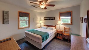 A bedroom with a bed, two bedside tables, a chair, a ceiling fan, and two windows. - Cole Bin - Ocracoke Island (Ocracoke)