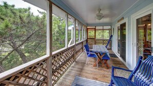 A covered porch with a table and chairs, large windows, and a view of trees. - Cole Bin - Ocracoke Island (Ocracoke)