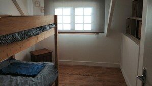 Huoneessa on kerrossänky, pieni puujakkara ja ikkuna, jossa on sälekaihtimet.