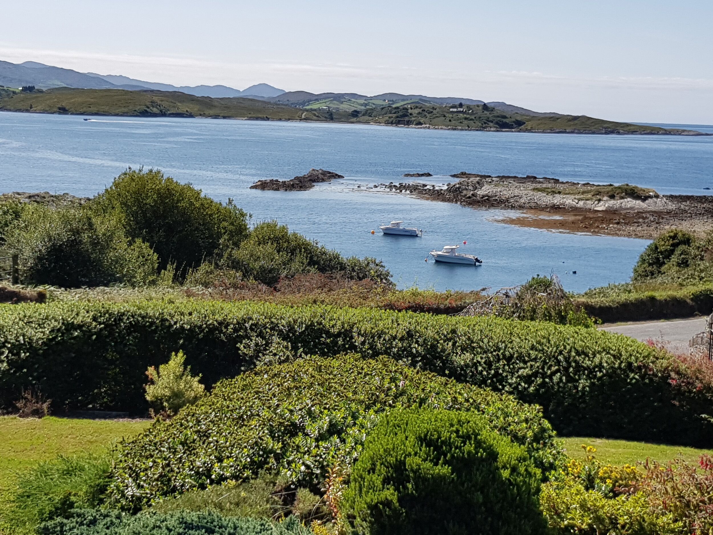 A coastal landscape with boats on the water, surrounded by greenery and hills in the background.