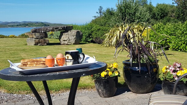Una mesa con tostadas, huevos y una taza, sobre un patio con una silla y plantas en macetas.