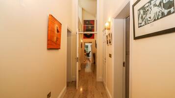 A hallway with artwork on the walls, a door on the right, and a view into another room.