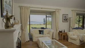 Un salón con vistas al mar, un sofá blanco, una mesa de centro de cristal y una lámpara.