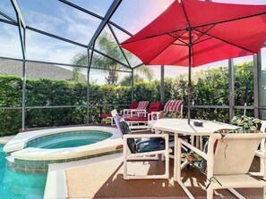 Een overdekte buitenterras met een jacuzzi, lounge stoelen en een tafel met parasols.