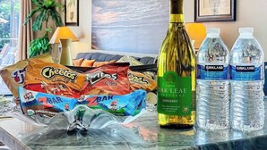 Une table avec des collations, une bouteille de vin et des bouteilles d’eau, dans une pièce offrant une vue sur l’océan.