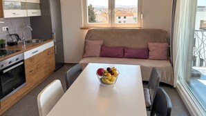 Ett kompakt kök med en matplats, en soffa med kuddar och en skål med frukt på bordet.