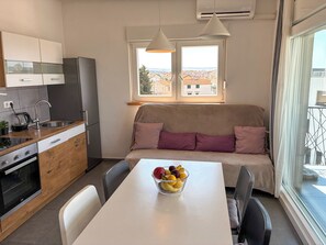 A compact kitchen with a dining area, a sofa with cushions, and a bowl of fruit on the table. - Summer holiday apartment- spacious sea view terrace- 2 min walk to the beach (Brodarica)