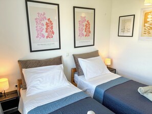 A hotel room with two beds, each with a pillow and a blanket, a nightstand with a lamp, and framed artwork on the wall. - Summer holiday apartment- spacious sea view terrace- 2 min walk to the beach (Brodarica)